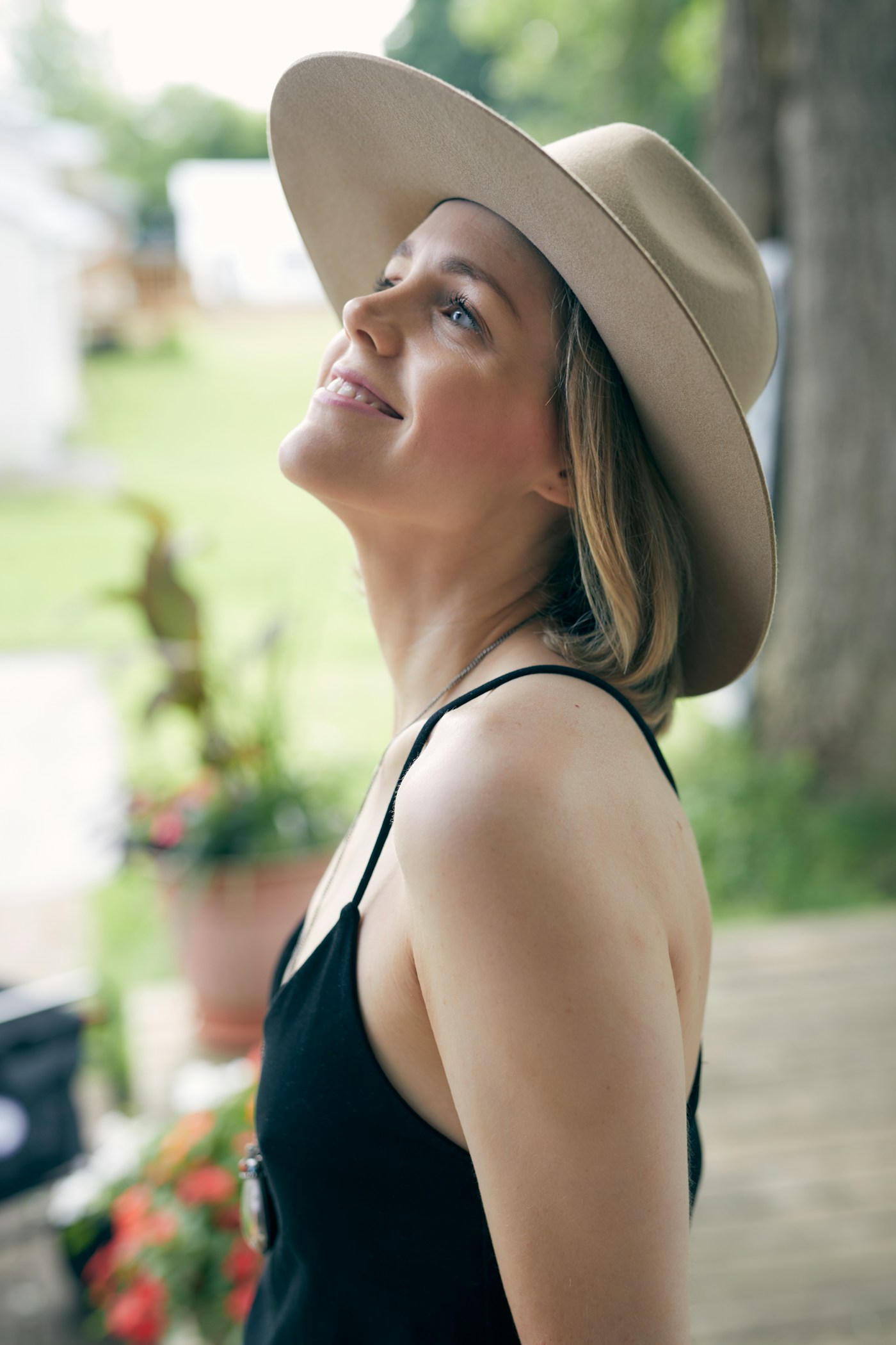 A woman wearing a hat standing in front of a tree.